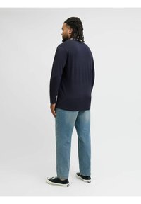 Dunkelblaues Langarmshirt mit lockerer Passform, kombiniert mit hellblauen Jeans und schwarzen Sneakern mit weißen Sohlen.