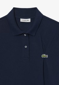 T-paita tummansinisestä puuvillasta, jossa on teksturoitu kangas, kolme nappia etuosassa ja vihreä krokotiililogo vasemmassa rinnassa.