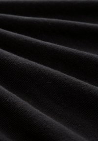 Nahaufnahme von schwarzem geripptem Stoff mit weicher Textur und parallel verlaufenden erhabenen Linien, die ein Wellenmuster bilden.