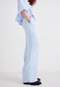 Pantalons larges bleu clair en tissu doux, avec des poches latérales et une texture lisse. Associé à un haut à manches courtes à carreaux.