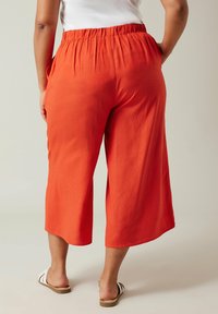 Culottes rouges avec une taille élastique, coupe décontractée et poches latérales, associées à des sandales à glissière rayées. Texture lisse et longueur mi-mollet.