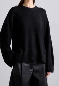 Musta ylikokoinen pehmeästä neuloksesta valmistettu paita, jossa resorit hihansuissa ja helmassa, pyöreä pääntie ja rento istuvuus. Yhdistetty mustiin nahkahousuihin.