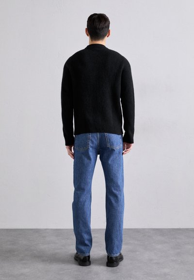 Μαύρο πλεκτό πουλόβερ με στρογγυλή λαιμόκοψη, σε συνδυασμό με μεσαίες μπλε ίσιες παντελόνες και μαύρα παπούτσια. Απλός σχεδιασμός, χωρίς ορατά μοτίβα.