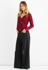 Cardigan cropped bordeaux con scollo a V e bottone dorato, abbinato a jeans neri a gamba larga a vita alta con tasche anteriori.