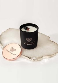 Candela nera in un contenitore opaco, con etichetta "CRYSTALLOVE black obsidian & oud." Il coperchio in metallo rosa oro metallizzato è appoggiato su una superficie di marmo lucida.