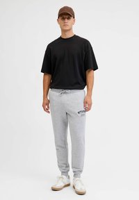 Czarna oversize'owa koszulka, szare spodnie dresowe z logo, jasne sneakersy z beżowymi akcentami oraz brązowa czapka. Prosty, sportowy design.
