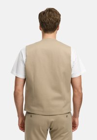 Beige ermeløs vest med glatt tekstur, baksømmene, og rund halslinning, brukt over en hvit t-skjorte. Enkelt og minimalistisk design.
