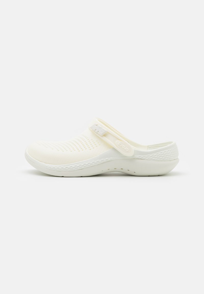 Sabot blanc en matériau flexible, avec un design perforé, une sangle ajustable et une semelle texturée pour une meilleure adhérence.