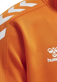 Orange sportsweatshirt med hvide chevron-striber på skulderen og et hvidt Hummel-logo på brystet.
