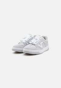 Grå semskede sneakers med hvite gummisåler og snørebånd. Har et minimalistisk design og en trekantet aksent på siden.