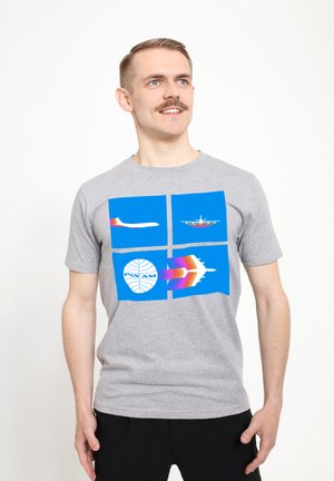 Grå kortærmet t-shirt med farverige luftfartsdesigns på en blå baggrund, med et rundt logo der siger "PAN AM."