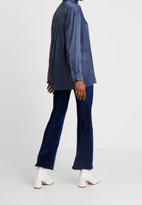 Navy blauwe zijdeachtige blouse met lange mouwen en knoopmanchetten, gecombineerd met ribbelige navy flared broeken en witte blokhak enkellaarsjes.