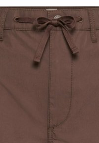 Close-up of brown pants waist with fabric drawstring tied in a bow through metal eyelets and visible stitching details.