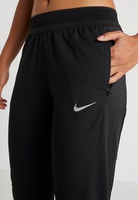 Czarne spodnie sportowe z elastycznym pasem, bocznymi kieszeniami i subtelnym logo Nike. Materiał ma gładką fakturę z perforowanymi detalami.