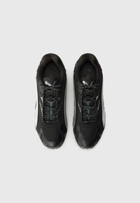 Zapatillas deportivas negras con parte superior de malla, cuello acolchado y acentos reflectantes. Presentan una suela texturizada negra y cordones con patrón.