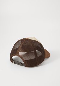 Ruskea verkko-trucker-lakki, jossa on yksivärinen beige etupaneeli, taivutettu lippa ja säädettävä napsautuskiinnitys. Tekstuuri kangas ja jämäkkä muotoilu.