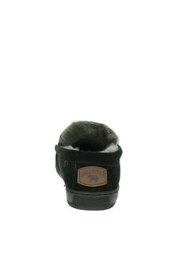 Pantoufle en suède noir avec doublure en fourrure douce, extérieur texturé et un patch en cuir marron avec le nom de la marque à l'arrière.