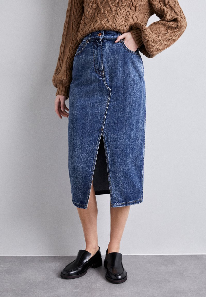 Jeanspencilkjole med frontsplitt, høyt liv, blå farge og klassisk fem-lommers design, parret med svarte slip-on sko.