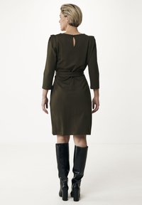 Olivgrön, knälång klänning med långa ärmar och en nyckelhålskärning bak. Matchad med höga, glänsande svarta knästövlar.