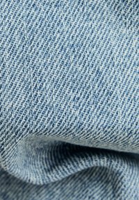 Denimtyg i ljusblått med ett subtilt diagonalt twillmönster, som visar en mjuk textur och lätta rynkor, vilket indikerar flexibilitet.