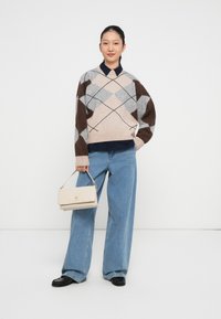 Maglione in misto lana argyle beige, grigio e marrone, abbinato a jeans a gamba larga e una borsa crema con chiusura dorata.