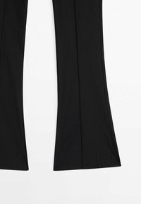 Pantalon noir évasé avec des coutures visibles courant le long de l'avant de chaque jambe, posé à plat sur un fond blanc.
