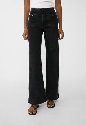 Sorte brede jeans lavet af denim med høj talje, der har to forlommer og sølvknapper. Tekstureret stof med synlige syninger.