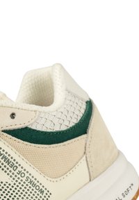 Baskets beiges et vertes avec une tige texturée, des accents en daim, une doublure en mesh et une semelle en caoutchouc avec un logo sur le côté.