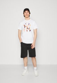 Camiseta blanca con un gráfico colorido de NY, pantalones cortos negros, zapatillas blancas y una gorra negra. Atuendo casual con un diseño simple y colores claros.