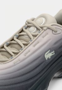 Baskets dégradées beige et grises avec une langue en mesh, de gros lacets beiges et un petit logo de crocodile sur le côté.