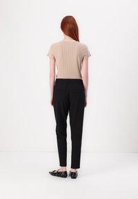 Beige ribbes T-skjorte med korte ermer kombinert med svarte skrudde bukser og svarte slip-on sko med metallisk øyelokkdetaljer.