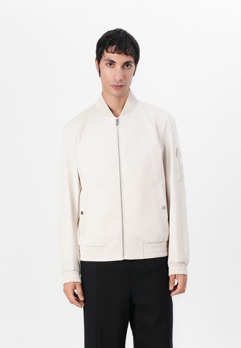 Light beige bomber jacket with a front zip closure, side pockets, ribbed collar, and elastic cuffs and hem. Smooth, matte finish.
