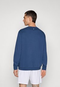 Felpa blu realizzata in morbido tessuto, con collo rotondo, maniche lunghe e un piccolo bottone decorativo sul retro del collo. Design con vestibilità rilassata.