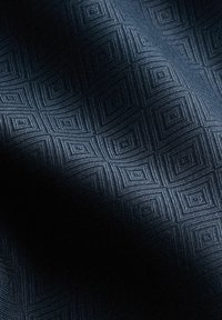 Tejido texturizado en azul marino oscuro que presenta un patrón geométrico de formas de diamante y líneas paralelas, creando un sutil efecto tridimensional.