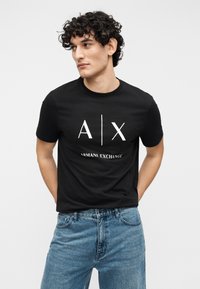 Svart bomulls-t-skjorte med hvit "A|X"-logo og teksten "ARMANI EXCHANGE", kombinert med lyseblå denimjeans.