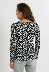 Chemise noire à manches longues avec un motif abstrait blanc. Fabriquée en tissu doux et texturé, elle possède un col rond et une coupe ajustée.
