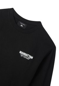 Felpa nera con collo a giro, caratterizzata da scritte ricamate bianche: "MANHATTAN IL TUO DESTINO È QUI IMPROVISA LA TUA MENTE." Texture semplice.
