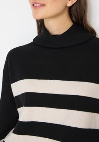 Pull en maille noir avec un col montant, présentant des rayures horizontales alternées en crème et noir pour un design contrasté.