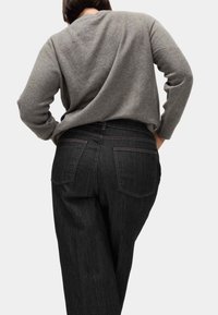 Pull en maille grise à coupe décontractée, associé à un jean en denim foncé avec deux poches arrière et des coutures contrastées.