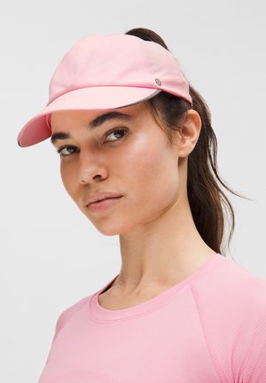 Mladá žena s růžovým kšiltem a sladěným růžovým sportovním tričkem, se svázanými vlasy, která se mírně dívá stranou.