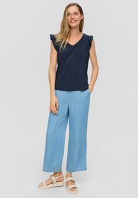 Granatowy top z dekoltem w serek i falbankami na rękawach, w połączeniu z jasnoniebieskimi spodniami o szerokich nogawkach. Uzupełniony beżowymi sandałami z plecionymi paskami.