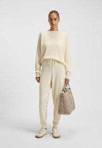 Krämfärgad stickad tröja och matchande joggers med dragsko. En kviltad beige väska med korta handtag. Vita sneakers med bruna sulor.
