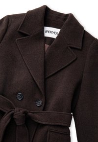 Cappotto in misto lana marrone con design doppiopetto, revers appuntiti, bottoni neri e cintura legata. Presenta tasche frontali e una texture liscia.