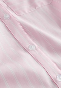 Artimųjų planas rausvos medžiagos su plonais baltais vertikaliais dryžiais, matomas sagomis užsegamas plokštelė ir krūtinės kišenės dalis.