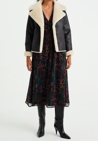 Svart jacka med fårskinnskrage och knapprapportering, lagd över en blommönstrad svart klänning, tillsammans med knähöga svarta höga stövlar.