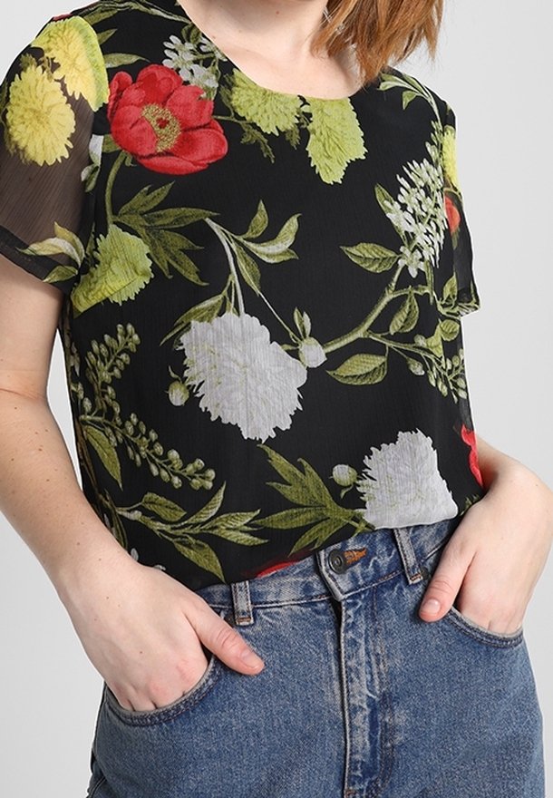 Blusa negra con estampado floral que presenta flores rojas, amarillas y blancas, de mangas cortas y un corte holgado. Combinada con jeans de tiro alto en azul.