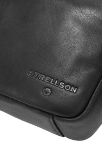 Črna usnjena torba z teksturirano površino. Na sprednji strani je vtisnjen logotip in simbol "STRELLSON". Ponuja sodoben dizajn in zaobljene robove.
