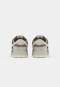 Nike tenisice u sivoj i smešanoj boji, s glatkim materijalom, podstavljenim okovratnikom i gumenim đonom s utorima. Minimalno brendiranje na peti.