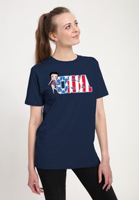 Marineblaues T-Shirt mit einem Grafiken eines Cartoon-Charakters und dem Text "USA" in Rot und Weiß, vor einem Hintergrund mit blauen Sternmustern.