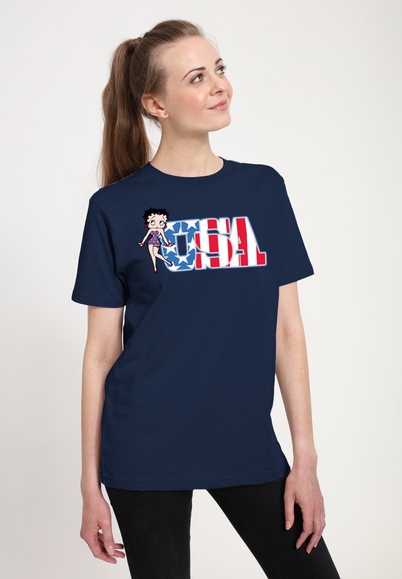 Marineblaues T-Shirt mit einem Grafiken eines Cartoon-Charakters und dem Text "USA" in Rot und Weiß, vor einem Hintergrund mit blauen Sternmustern.